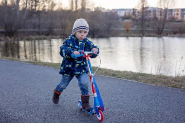 Güneşli bir bahar gününde parkta scooter süren tatlı bir çocuk.