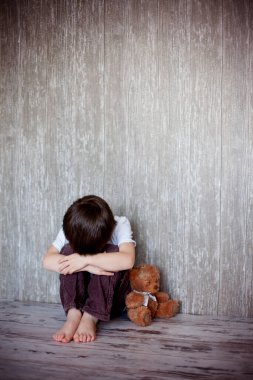 Genç çocuk, oturup onun oyuncak ayı ile yere, onun gözlerinde hüzün