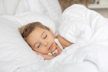 Güzel sarışın çocuk, oğlum, oyuncak ayıyla yatakta uyuyor, örgü örüyor.