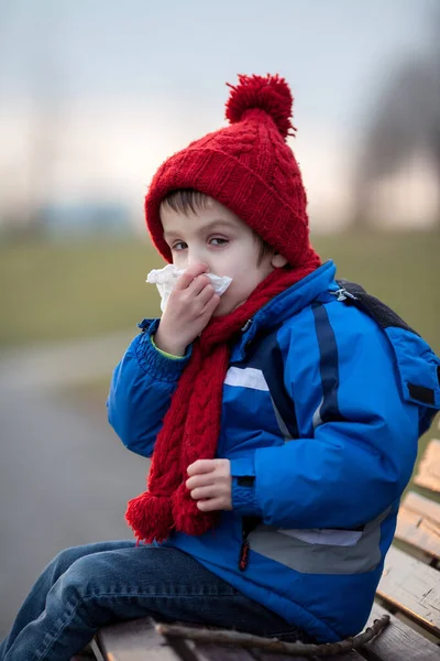 打喷嚏 擤鼻涕室外阳光明媚的冬日 坐在长凳上的小男孩 — 图库照片