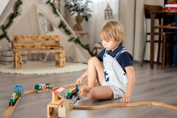 Sevimli sarışın çocuk, evdeki renkli trenlerle ve demiryollarıyla oynuyor.