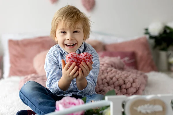 かわいいブロンドの子供 就学前の男の子 ハートの形でピンクのドーナツを食べる バレンタインのために作られた バレンタインの背景 — ストック写真