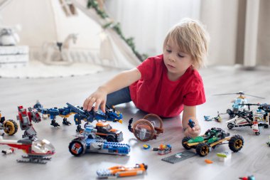 Tatlı çocuk, sarışın çocuk, Colofrul plastik bloklarla oynuyor, inşaat oyuncakları, araba ve uçak yapıyor.