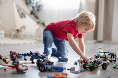 Tatlı çocuk, sarışın çocuk, Colofrul plastik bloklarla oynuyor, inşaat oyuncakları, araba ve uçak yapıyor.