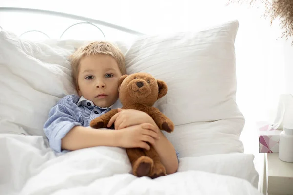 可爱的金发学龄前儿童和泰迪熊 躺在卧床病了 阳光灿烂的卧室里 — 图库照片