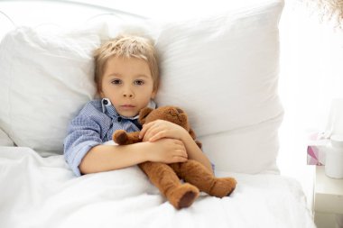 Oyuncak ayıyla tatlı sarışın anaokulu çocuğu, hasta yatıyor, güneşli yatak odasında.