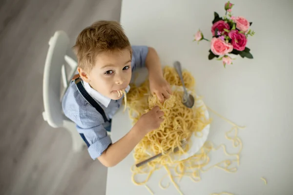 かわいい就学前の子供ブロンドの男の子家でスパゲティを食べてどこでも混乱させる面白い瞬間 — ストック写真