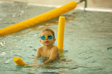 Çocuk, kapalı havuzda bir grup çocuktan yüzme dersleri alıyor, öğrenmenin tadını çıkarıyor.
