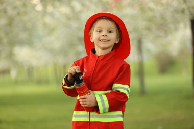 Little toddler child with fireman costume in park, pretending to be real fireman, playing on sunset