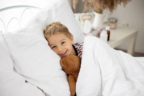 甘いですブロンド就学前の子供とともにテディベア ベッドで横たわっ病気 日当たりの良いベッドルーム — ストック写真