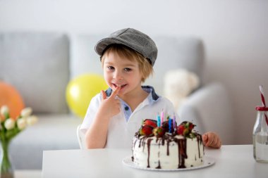 Dört yaşında sarışın bir çocuk, anaokulu çocuğu, doğum gününü evde çilekli ve çikolatalı ev yapımı pastayla kutluyor.