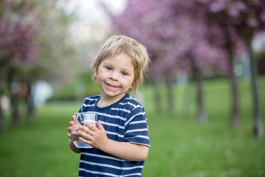 Güzel sarışın çocuk, evlat, sıcak bir yaz gününde parkta su içiyor.