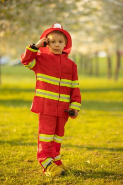 Little toddler child with fireman costume in park, pretending to be real fireman, playing on sunset