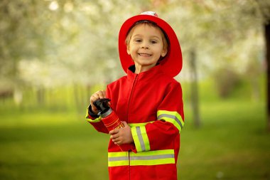 Little toddler child with fireman costume in park, pretending to be real fireman, playing on sunset