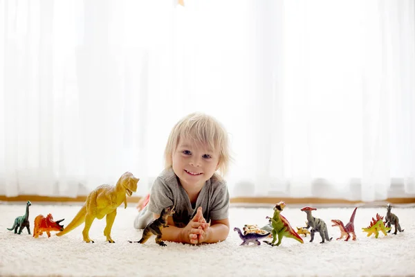 金发碧眼的蹒跚学步的孩子 在家里和恐龙玩耍 背光柔嫩漂亮 — 图库照片