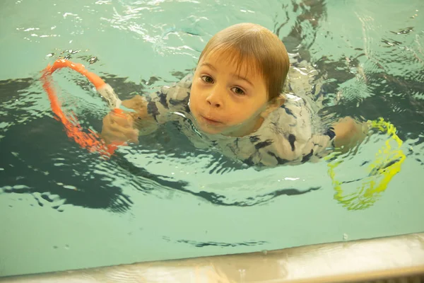 Young child, taking swimming lessons, swimming in clothing, learning how to survive in case of accidental falling into water. pool lessons