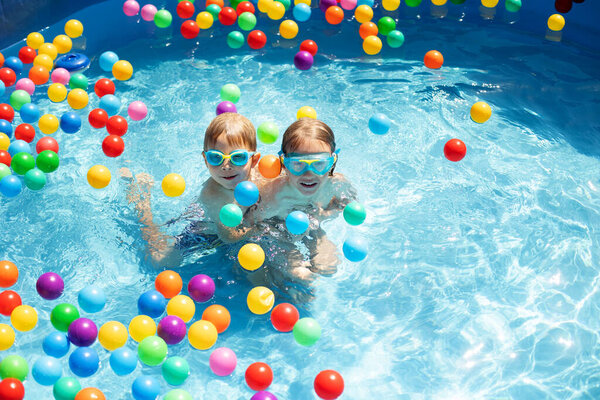 Young child, swimming in the summer in a pool full of colorful balls, enjoying beautiful sunny weather outdoors