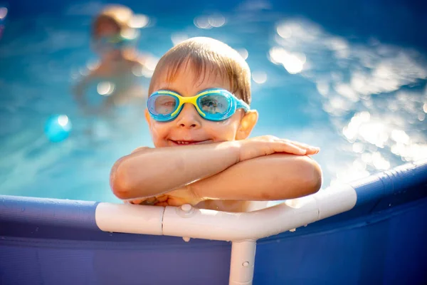 Young child, swimming in the summer in a pool full of colorful balls, enjoying beautiful sunny weather outdoors