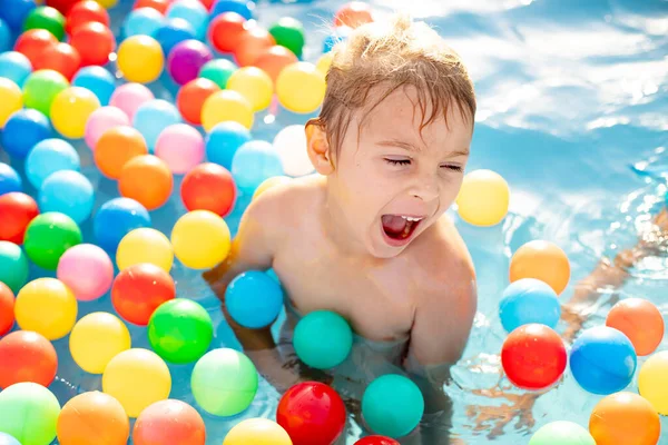 Young child, swimming in the summer in a pool full of colorful balls, enjoying beautiful sunny weather outdoors