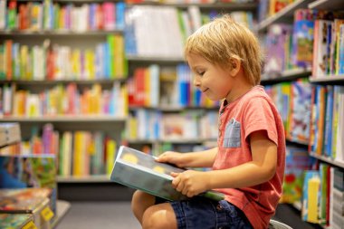 Cute preschool child, sitting in a bookstore, looking at books on summer day