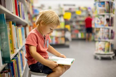Cute preschool child, sitting in a bookstore, looking at books on summer day