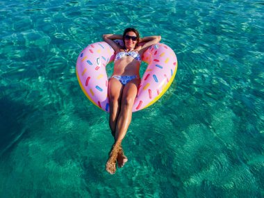 Picture with drone of people, floating on inflatable colorful rings in the sea