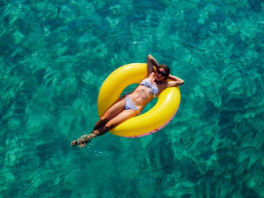 Picture with drone of people, floating on inflatable colorful rings in the sea