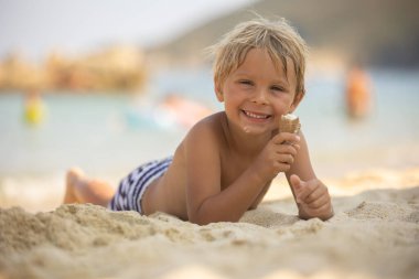 Happy child, boy eating ice cream  on the beach, enjoying summer, playing. Halkidiki, Greece