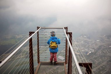 Child in blue jacket looking down from Rampestreken in Andalsnes. Norway on a very foggy day