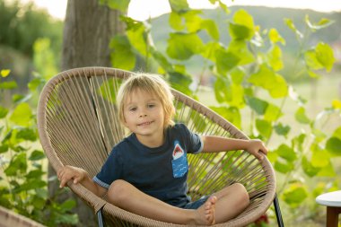 Boy, child on holida, sitting on summer chair in garden, smiling