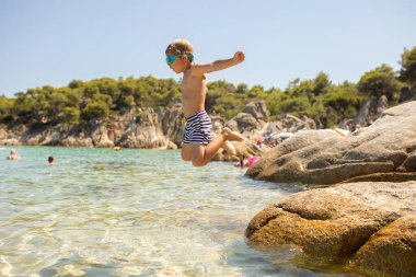 Happy toddler child on the beach, enjoying summer, playing, juming in the water. Halkidiki, Greece