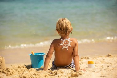 Happy child, blond boy on the beach with applied sun screen,  enjoying summer, playing. Halkidiki, Greece