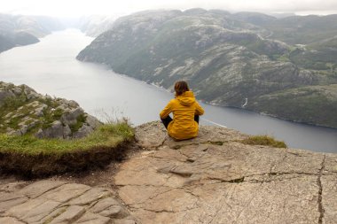 Family, enjoying the hike to Preikestolen, the Pulpit Rock in Lysebotn, Norway on a rainy day, toddler climbing with his pet dog the one of the most scenic fjords in Norway