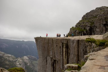Family, enjoying the hike to Preikestolen, the Pulpit Rock in Lysebotn, Norway on a rainy day, toddler climbing with his pet dog the one of the most scenic fjords in Norway