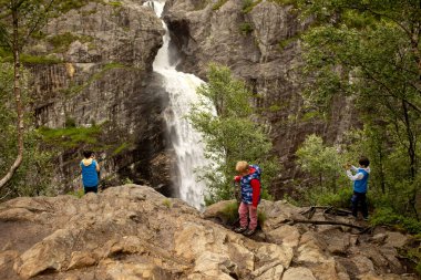 Happy european family with kids and dog, enjoying the hike to Manafossen waterfall summertime on a cold day