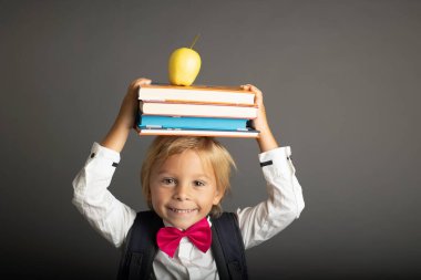 Cute preschool blond child, boy, holding books and notebook, apple, wearing glasses, ready to go to school