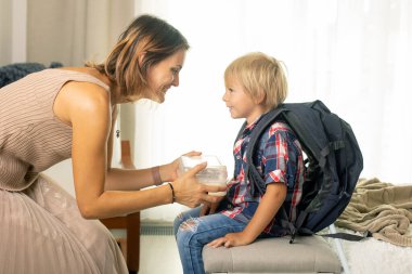Mother, sending her firstgrader boy to school, first day at school, giving him books and a box with snack at home