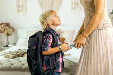 Mother, sending her firstgrader boy to school, first day at school, giving him books and a box with snack at home