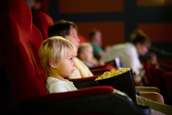 Cute child, boy, watching movie in a cinema, eating popcorn and enjoying the film