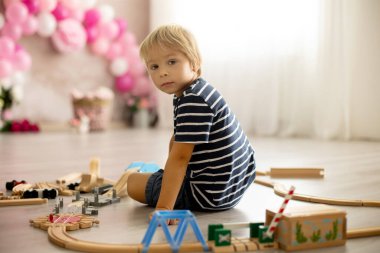 Cute child, blond toddler boy, playing with wooden trains at home