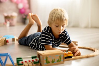 Cute child, blond toddler boy, playing with wooden trains at home