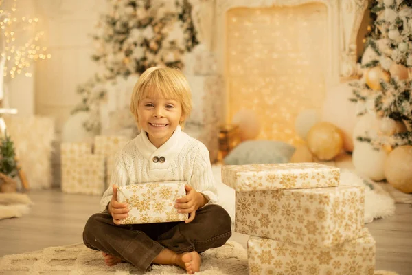可爱的金发幼儿学龄前男孩 阅读一本书 并在圣诞节打开礼物舒适的家 灯和装饰 — 图库照片