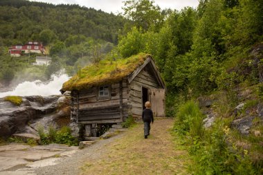 Amazing little wooden small house next to a waterfall on the dock of Hellesylt, child playing in the house, looking out of the window