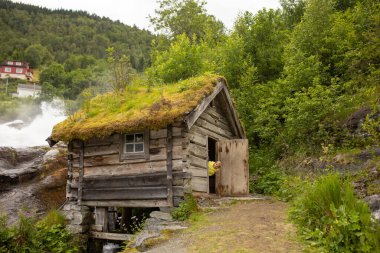 Amazing little wooden small house next to a waterfall on the dock of Hellesylt, child playing in the house, looking out of the window
