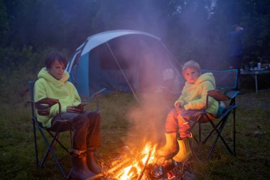 Kids, sitting around campfire at night, enjoying wild camping, family vacation in Norway