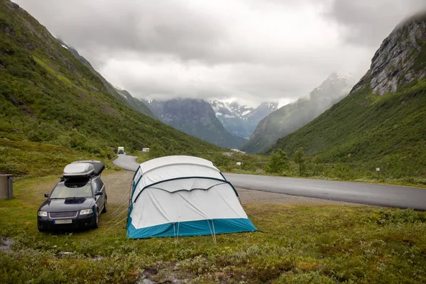 People, camping wild in Norway in high mountains, snow, cold, fog at night, pitched tent next to a car near the road