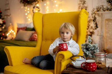 Tatlı çocuk, oğlum, Noel için süslü bir odada sarı bir koltukta oturuyor, rahat bir yer.
