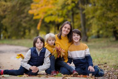 Mutlu bir aile, çocuklu bir anne, sonbahar resimleri parkta çekiliyor, çocuklar oyun oynuyor.