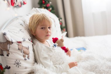 Güzel sarışın çocuk, ateşi olan hasta çocuk, Noel 'de yatakta yatıyor, öksürüyor ve burnu akıyor.