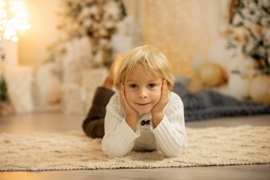 Tatlı sarışın anaokulu çocuğu, kitap okuyor ve Noel 'de rahat evde hediyesini açıyor, ışıklar ve süslemeler.